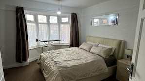 Un dormitorio con cama, cortinas en la ventana, un radiador, una mesita de noche y un espejo en la pared.