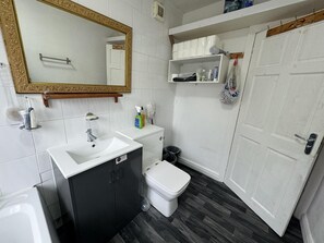 A bathroom with a white sink, black cabinets, a white toilet, a mirror with a gold frame, and a shelf with toiletries. - Charming Stoke House With 2 Nice Bedrooms (Stoke-on-Trent)