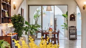Un coin repas avec une table dressée pour quatre personnes, entouré de plantes en pot, et une vue sur l’extérieur grâce à de grandes portes vitrées.