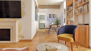 Una sala de estar con chimenea, televisor, estantería y comedor con sillas y mesa.