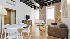 A spacious living area with a wooden floor, a white dining table with chairs, a sofa, and a television on a wooden cabinet. - Spagna Charme - One Bedroom Apartment, Sleeps 4 (Rome)