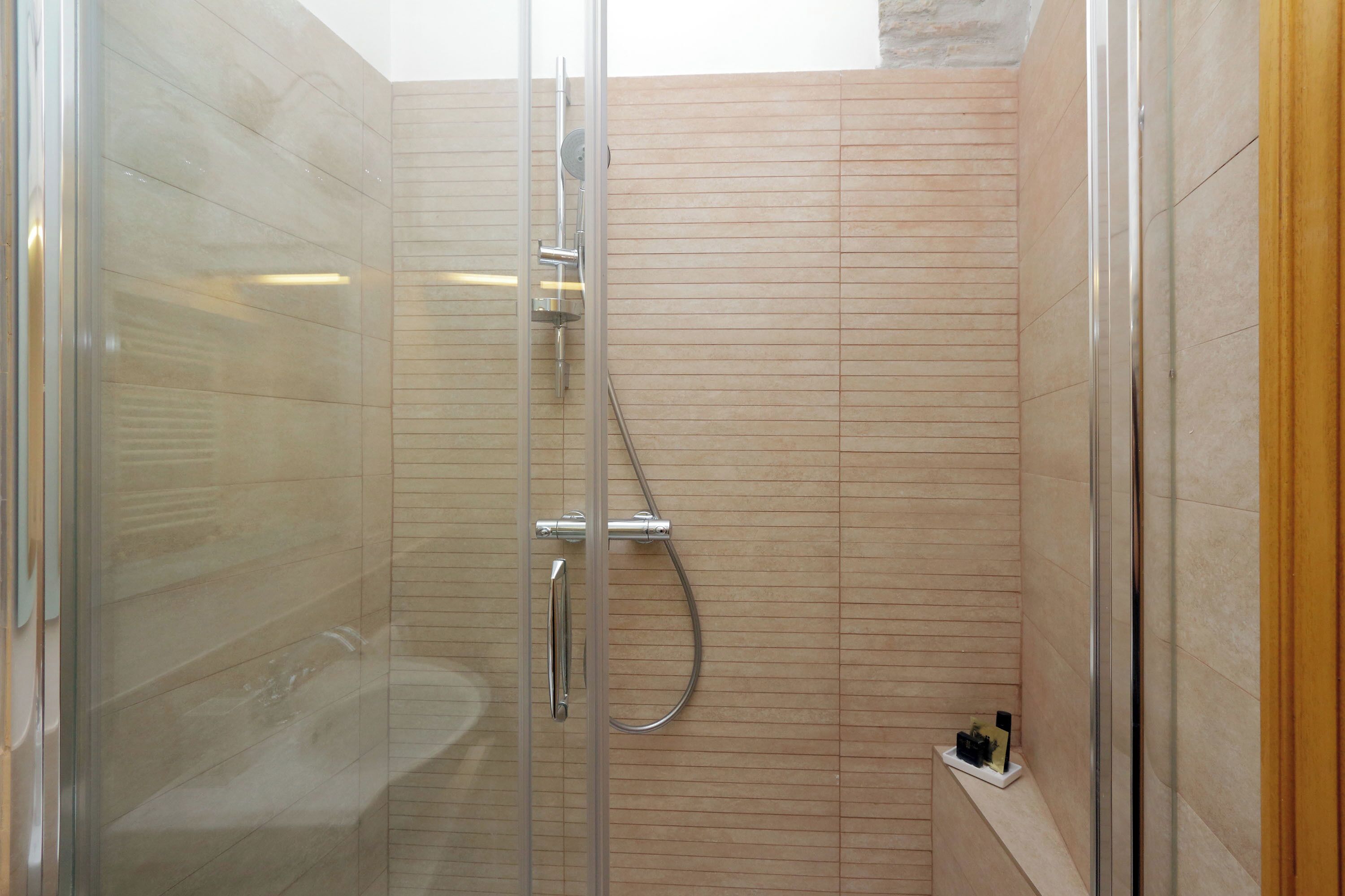 A glass-enclosed shower with a handheld showerhead and a wall-mounted faucet.