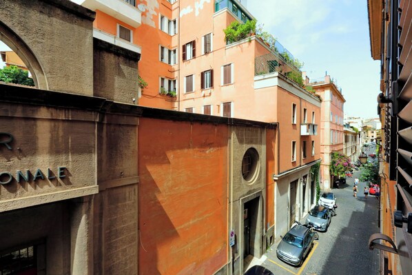 A narrow street with parked cars and buildings with balconies.