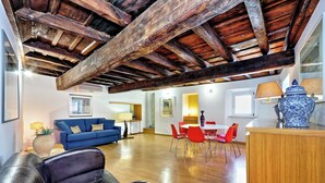 Un salón amplio con techo de madera, un sofá azul, sillas rojas y una mesa de comedor.