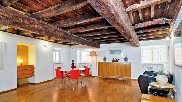 Una habitación amplia con suelo de madera, una zona de comedor con sillas rojas, un mueble de madera y un sillón de cuero negro.