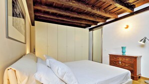 Un dormitorio con cama, vigas de madera en el techo, un aparador y una lámpara de pared.