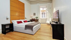 Une chambre moderne avec un grand lit, un bureau, une télévision et une vue sur un immeuble par la fenêtre.