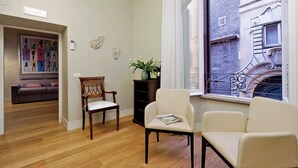 Un salon avec un plancher en bois, un canapé, une chaise en bois et une fenêtre donnant sur un immeuble.