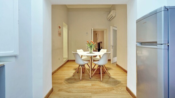 Une cuisine compacte avec un coin repas, comprenant un réfrigérateur moderne, une table ronde avec des chaises et un vase rempli de fleurs.