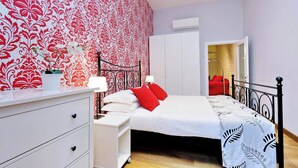 Une chambre à coucher avec un lit, une commode blanche et un mur orné d’un motif rouge et blanc.