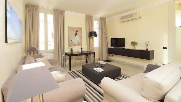 A modern living room with a sofa, a coffee table, a TV, and a dining area with a table and chairs.