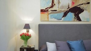 A bedroom with a bed, a nightstand, a lamp, and a painting on the wall.