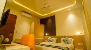 A hotel room with a bed, a desk, a chair, a TV, and an air conditioning unit. - Familia Hotel and Banquets (Lucknow)