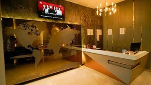 A reception area with a television mounted on the wall, a desk with a computer, and a decorative wall with a globe and abstract art. - Familia Hotel and Banquets (Lucknow)