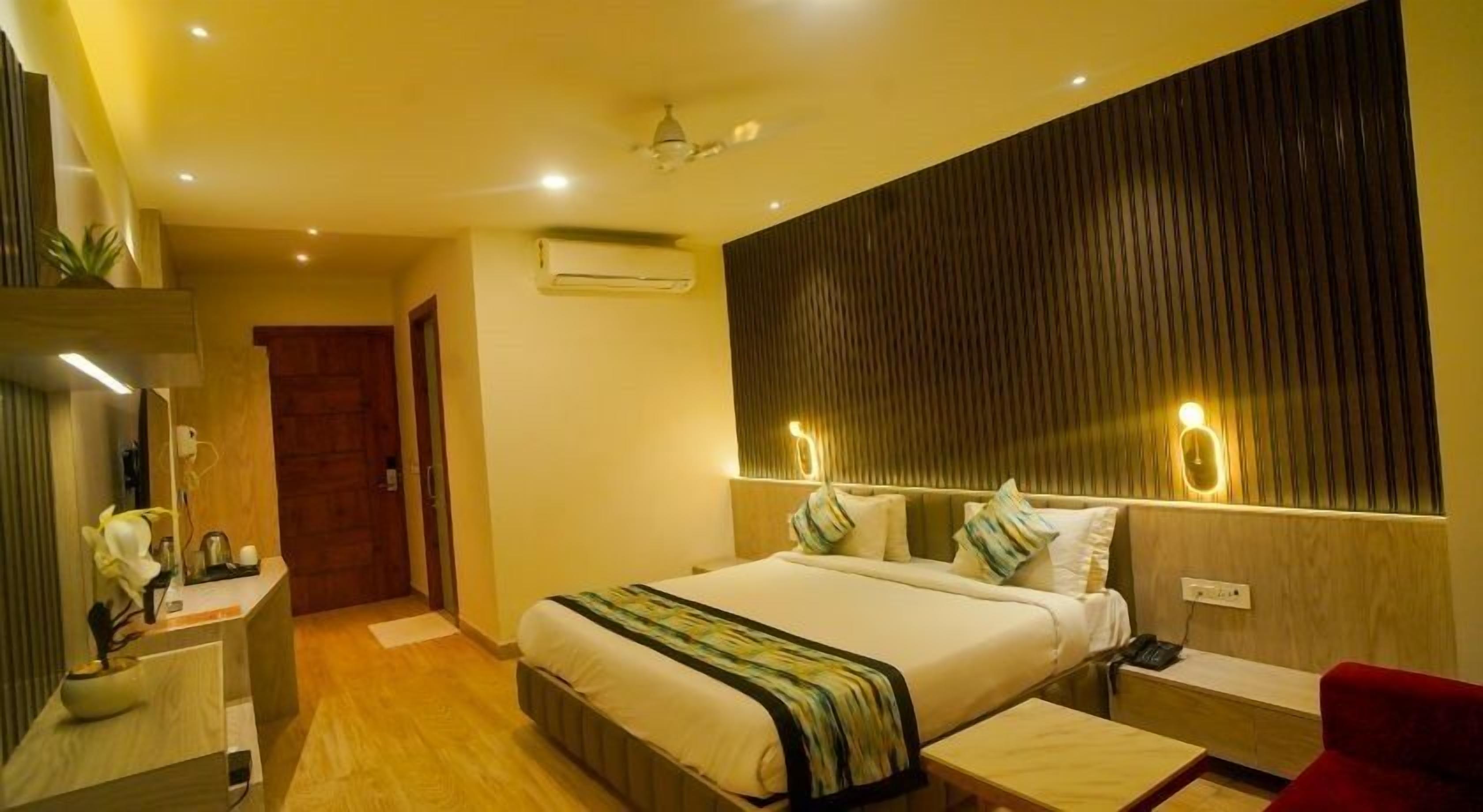 A hotel room with a large bed, bedside tables, a red chair, and a wooden headboard.