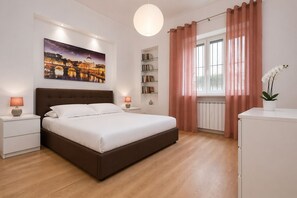 Um quarto moderno com uma cama grande, luminárias de cabeceira, uma estante, uma janela com cortinas e uma pintura de paisagem urbana na parede.