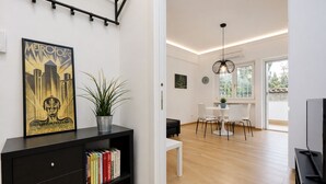 A modern living room with a black entertainment unit, a dining area with a white table and chairs, and a large window providing natural light. - Cozy Domar - Two Bedroom Apartment, Sleeps 6 (Rome)