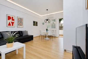 Una sala de estar moderna con un sofá negro, una mesa de centro blanca y un televisor.