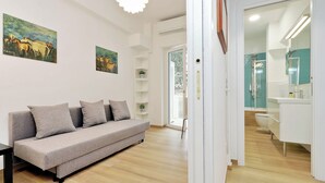 A modern living room with a grey sofa, a coffee table, and two paintings on the wall. There is a door leading to a bathroom with a white sink and mirror. - Cozy Domar - Two Bedroom Apartment, Sleeps 6 (Rome)