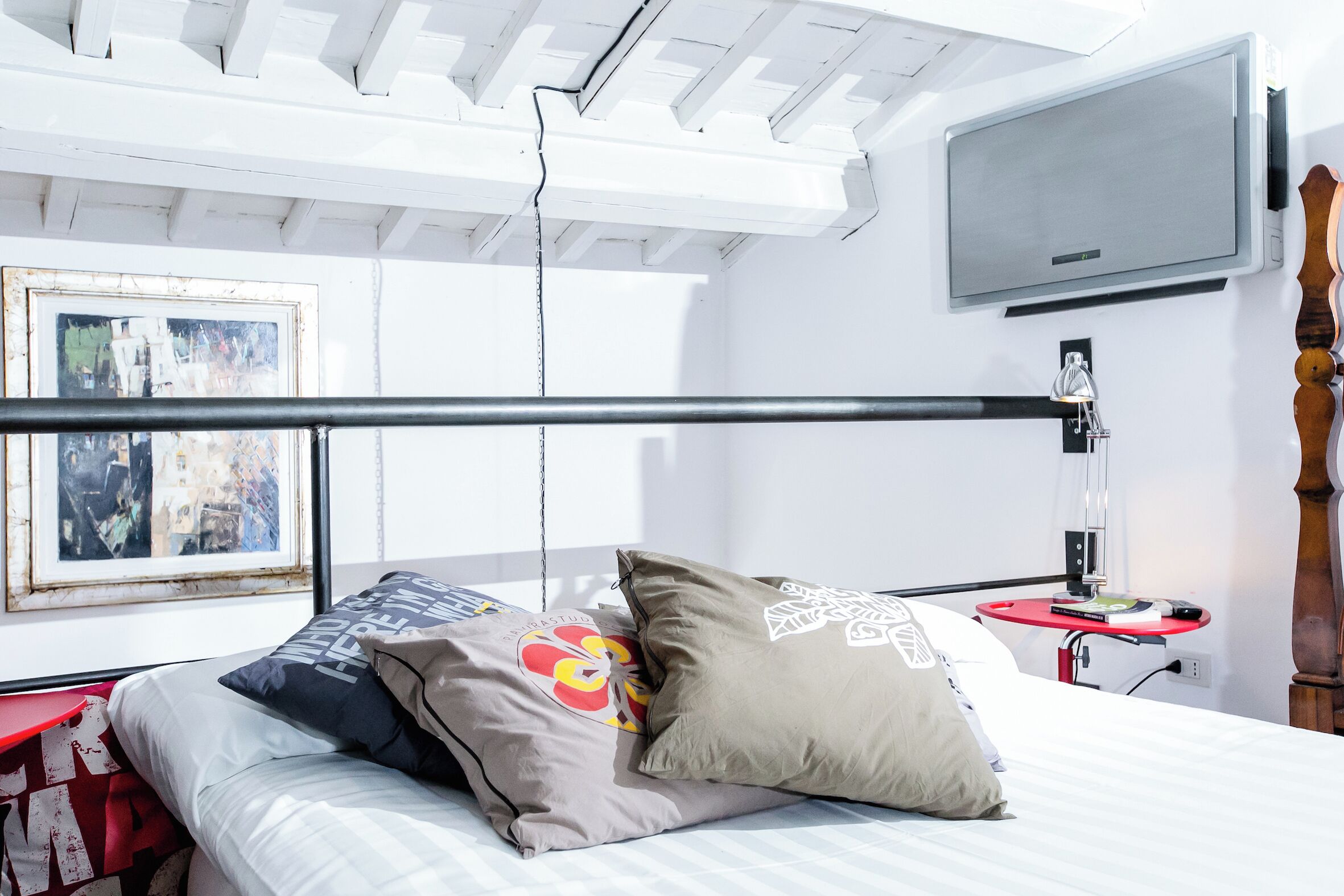 A bedroom with a bed, pillows, a TV, and a small table with a lamp.