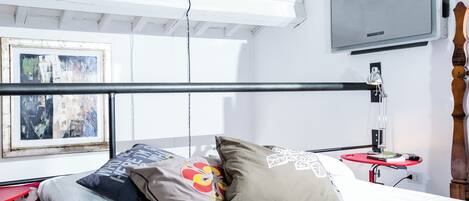 A bedroom with a bed, pillows, a TV, and a small table with a lamp.
