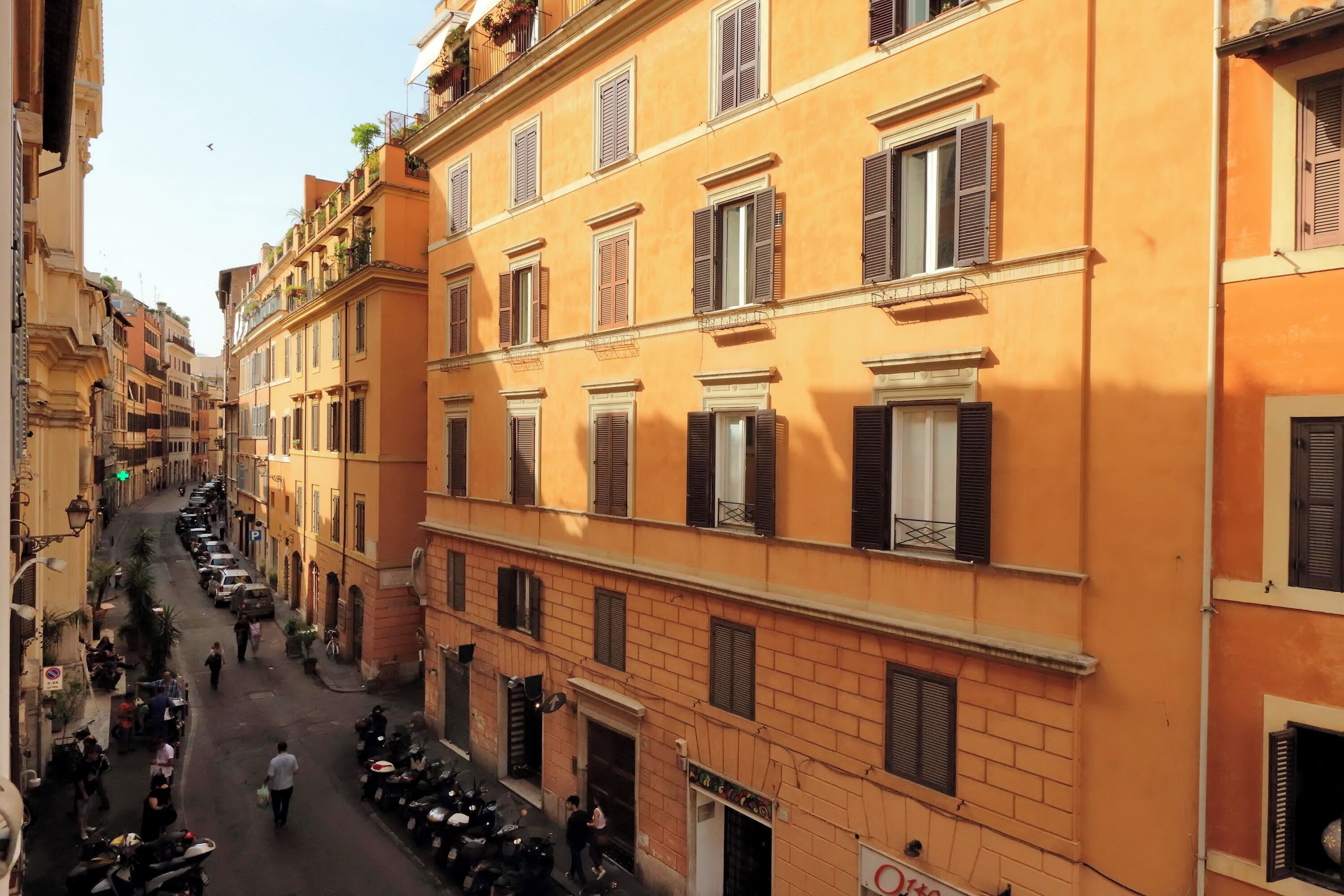 A narrow street lined with multi-story buildings, featuring balconies and shutters.