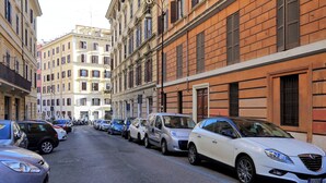 Une rue bordée de voitures garées et d’immeubles dotés de balcons et de volets.