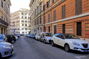 Une rue bordée de voitures garées et d’immeubles dotés de balcons et de volets.