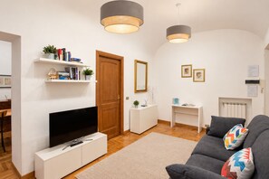 Un salon moderne avec un téléviseur à écran plat, un canapé gris agrémenté de coussins colorés, une porte en bois et une console blanche.