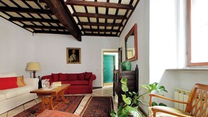 Ein Wohnzimmer mit weißem Sofa, rotem Sofa, Couchtisch aus Holz, gemusterten Teppichen, einem Holzstuhl und einer grünen Tür im Hintergrund.