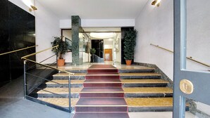 Una escalera con escalones de mármol y una alfombra roja que conduce a una puerta con picaporte de latón.