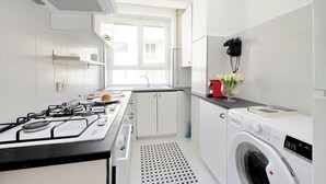 Una cocina moderna con armarios blancos, estufa a gas, horno empotrado, pileta y lavadora.