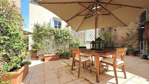 An outdoor patio with a wooden table and chairs, a large umbrella, and potted plants.