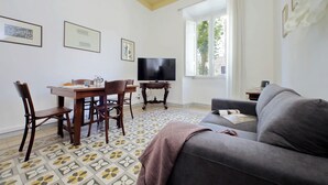 A living room with a sofa, a TV, a dining table with chairs, and a patterned floor. - Cozy Merulana - Two Bedroom Apartment, Sleeps 4 (Roma)