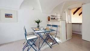 Un coin repas avec une table dressée pour deux personnes, des chaises bleues, un vase rempli de fleurs et un tableau accroché au mur.
