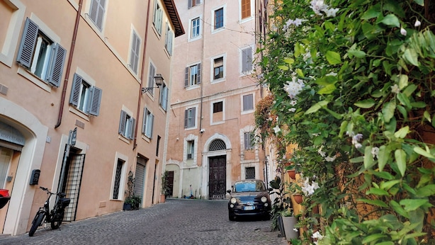 Une ruelle étroite pavée, bordée d’immeubles aux volets fermés, avec une voiture garée.