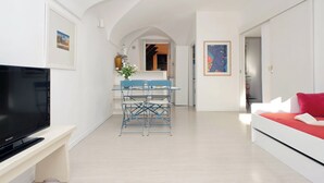 Un salon moderne doté d’un téléviseur à écran plat, d’un coin repas avec une table et des chaises, et d’un lit agrémenté d’un coussin rouge.