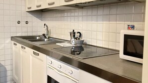 Une cuisine moderne avec des armoires blanches, un évier en acier inoxydable, un four encastré et un four à micro-ondes.