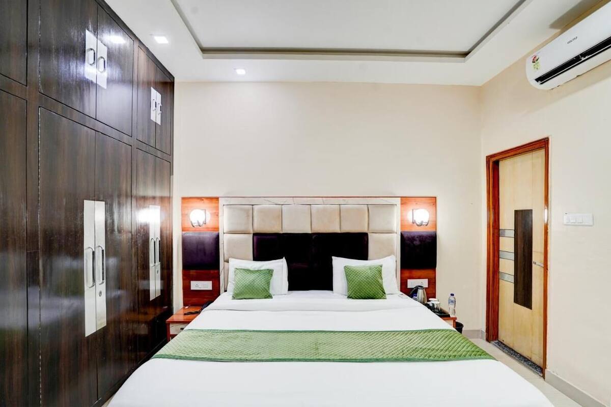 A hotel room with a large bed, wardrobe, bedside table, and an air conditioning unit.