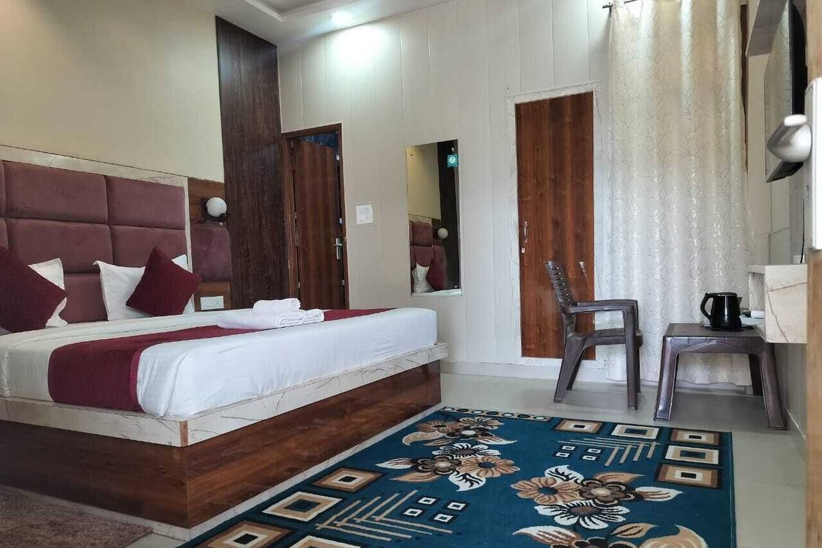 A hotel room with a bed, a chair, a small table with a coffee pot, and a patterned rug.