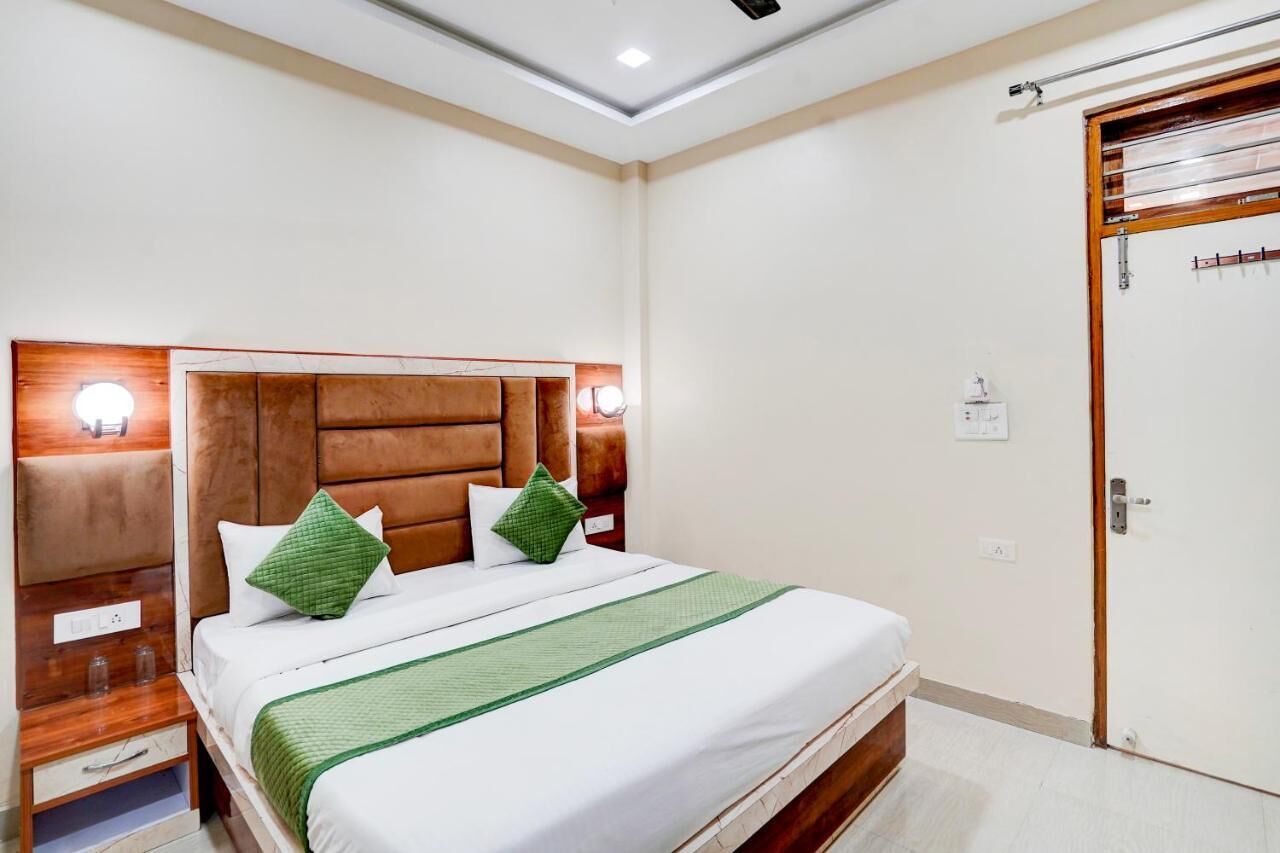 A hotel room with a wooden headboard, a bed with white bedding and green accents, a nightstand, and a door with a wooden frame.