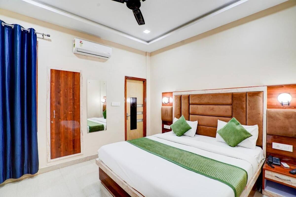 A hotel room with a large bed, a wooden headboard, a nightstand, a mirror, and an air conditioning unit.
