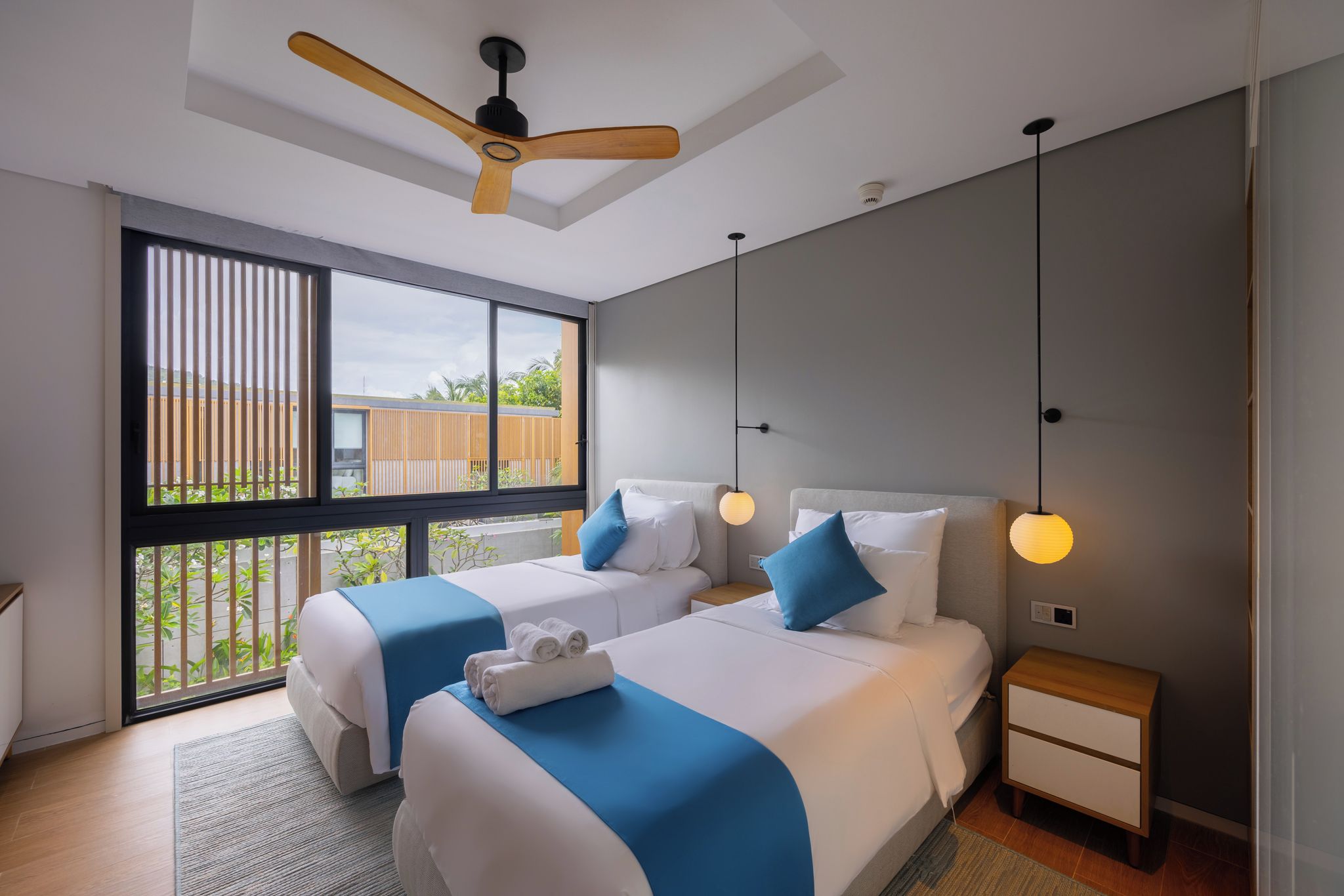 A modern hotel room with two beds, a ceiling fan, bedside lamps, and a view of the outdoors.