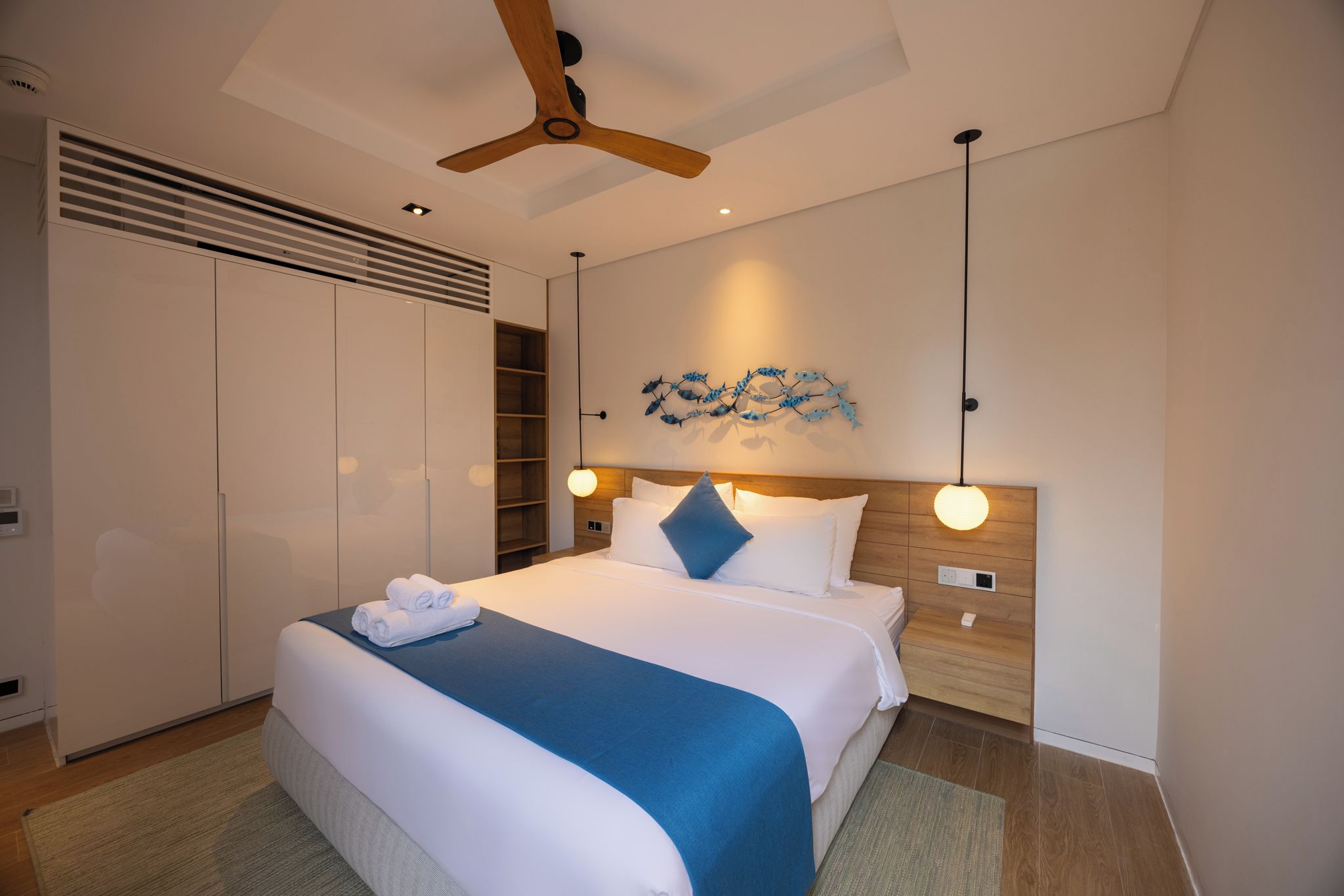 A modern hotel room with a large bed, a ceiling fan, a wall-mounted artwork, and a built-in wardrobe.