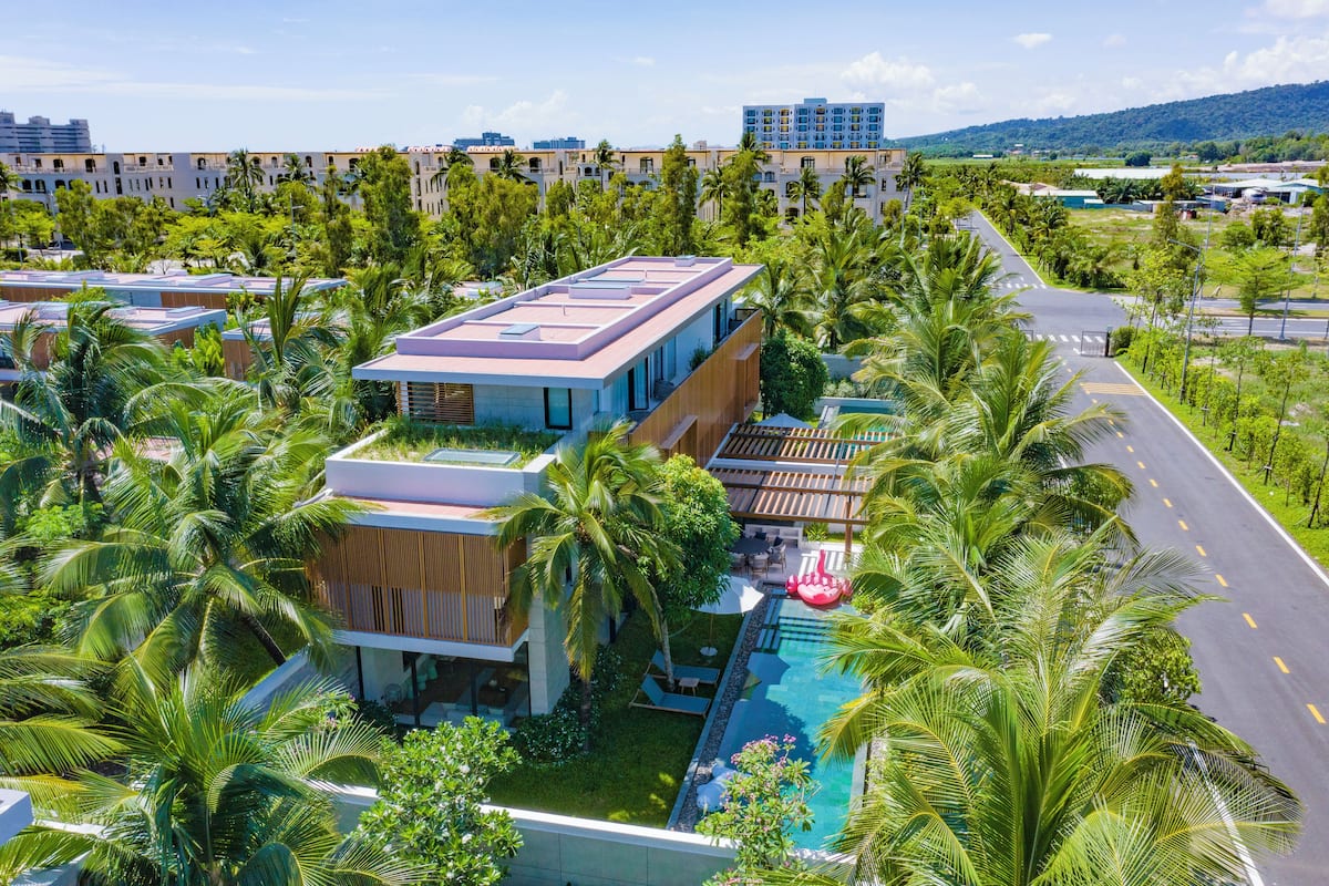 A modern hotel with a rooftop pool, surrounded by lush greenery and palm trees.