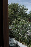 Vista de un balcón con diversas plantas y flores, una mesa de vidrio y una pared blanca.