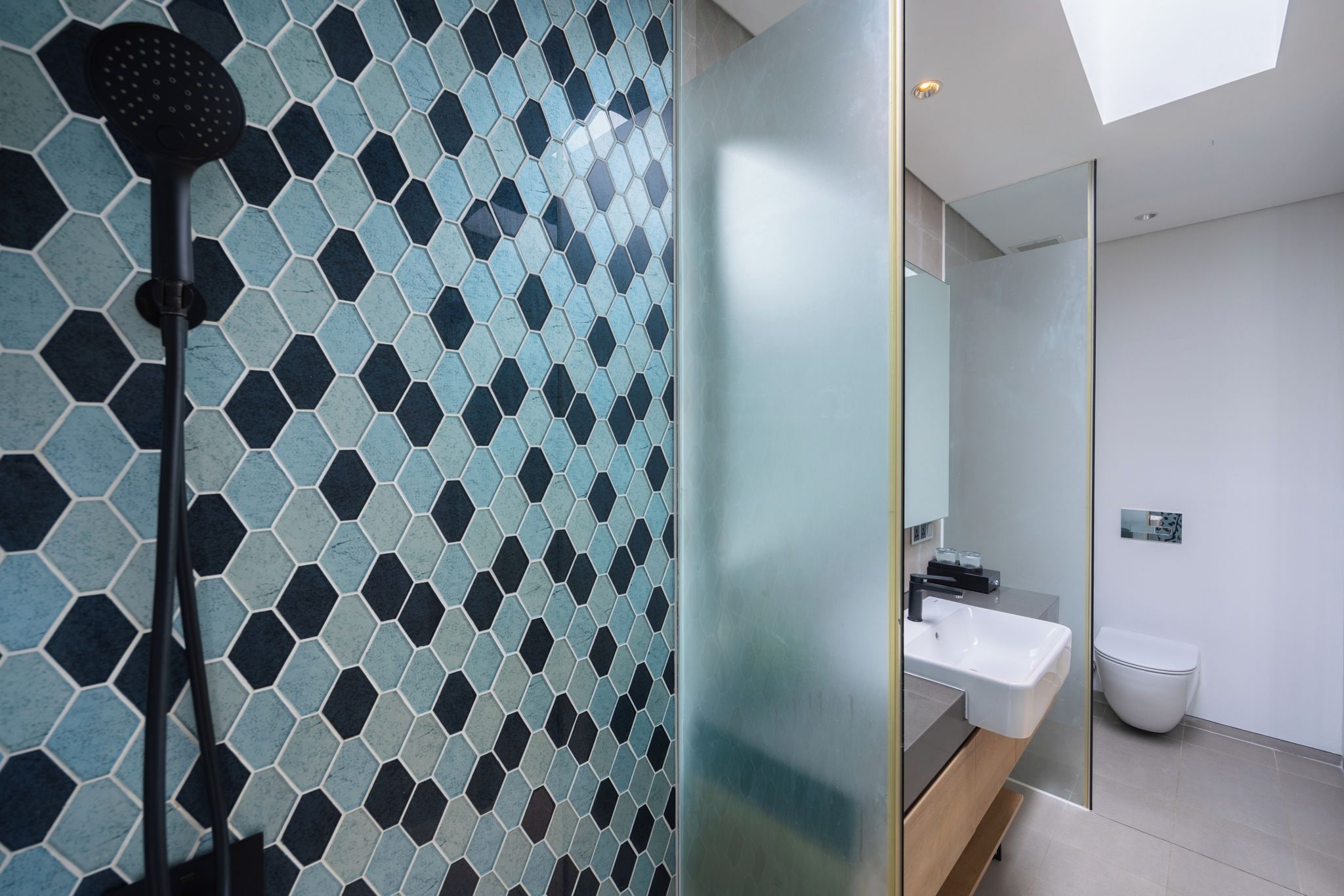 A modern bathroom with a hexagonal tile backsplash, a glass shower enclosure, and a white sink.