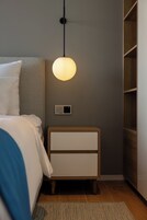 Un dormitorio con cama, mesita de noche, lámpara de pared y una luminaria.