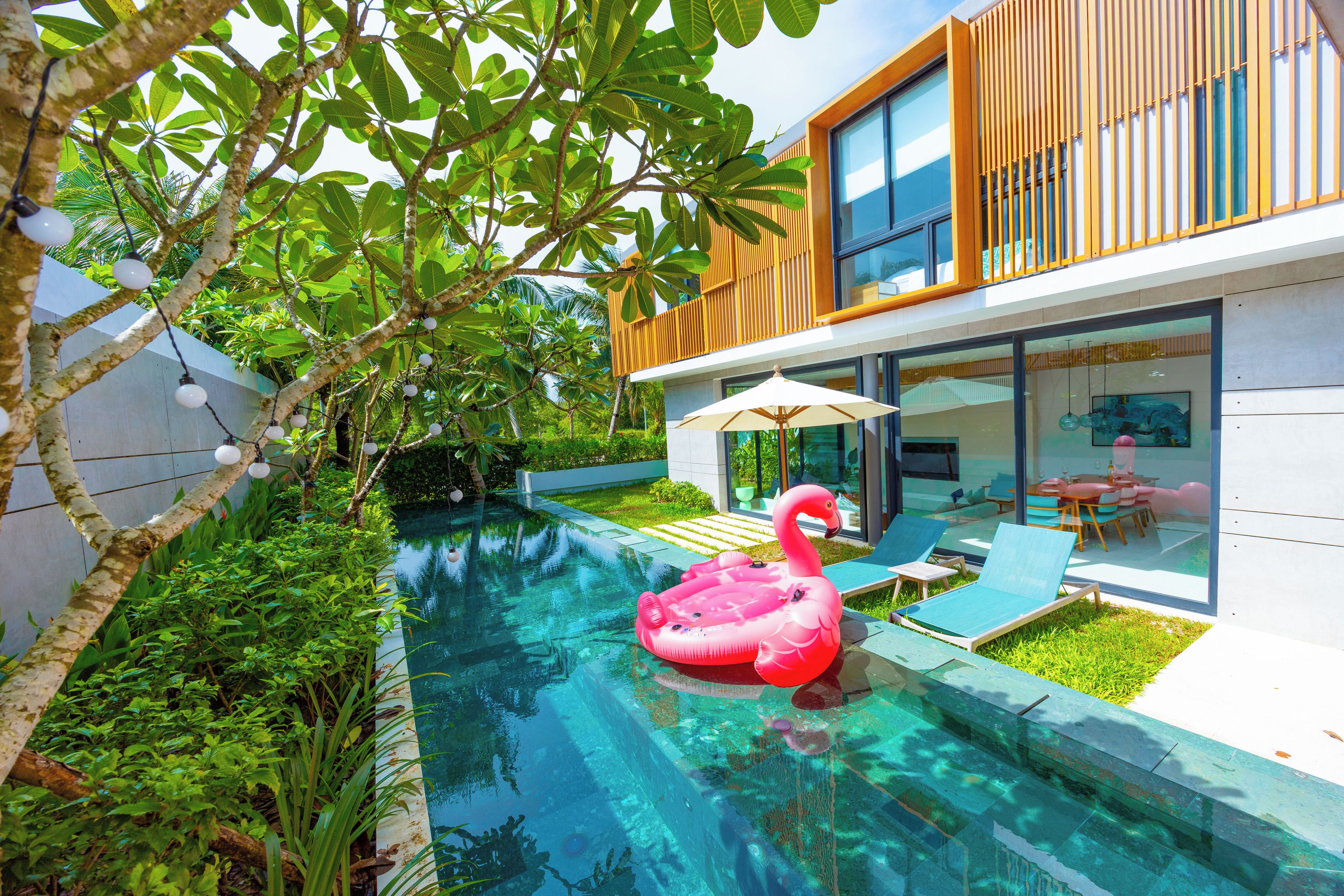 A modern house with a swimming pool, a flamingo float, and a glass door leading to a patio with a table and chairs.