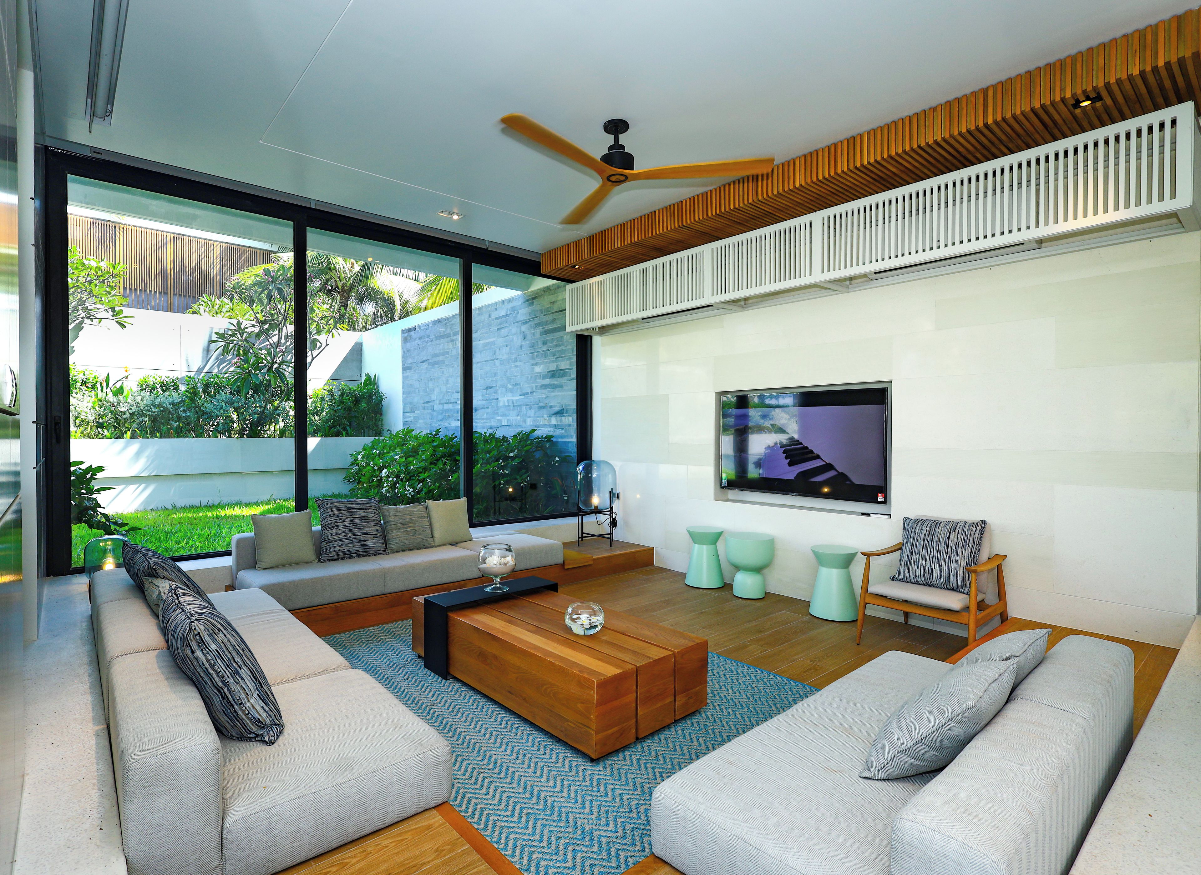Una sala de estar moderna con televisor grande, asientos cómodos y vista a un jardín.